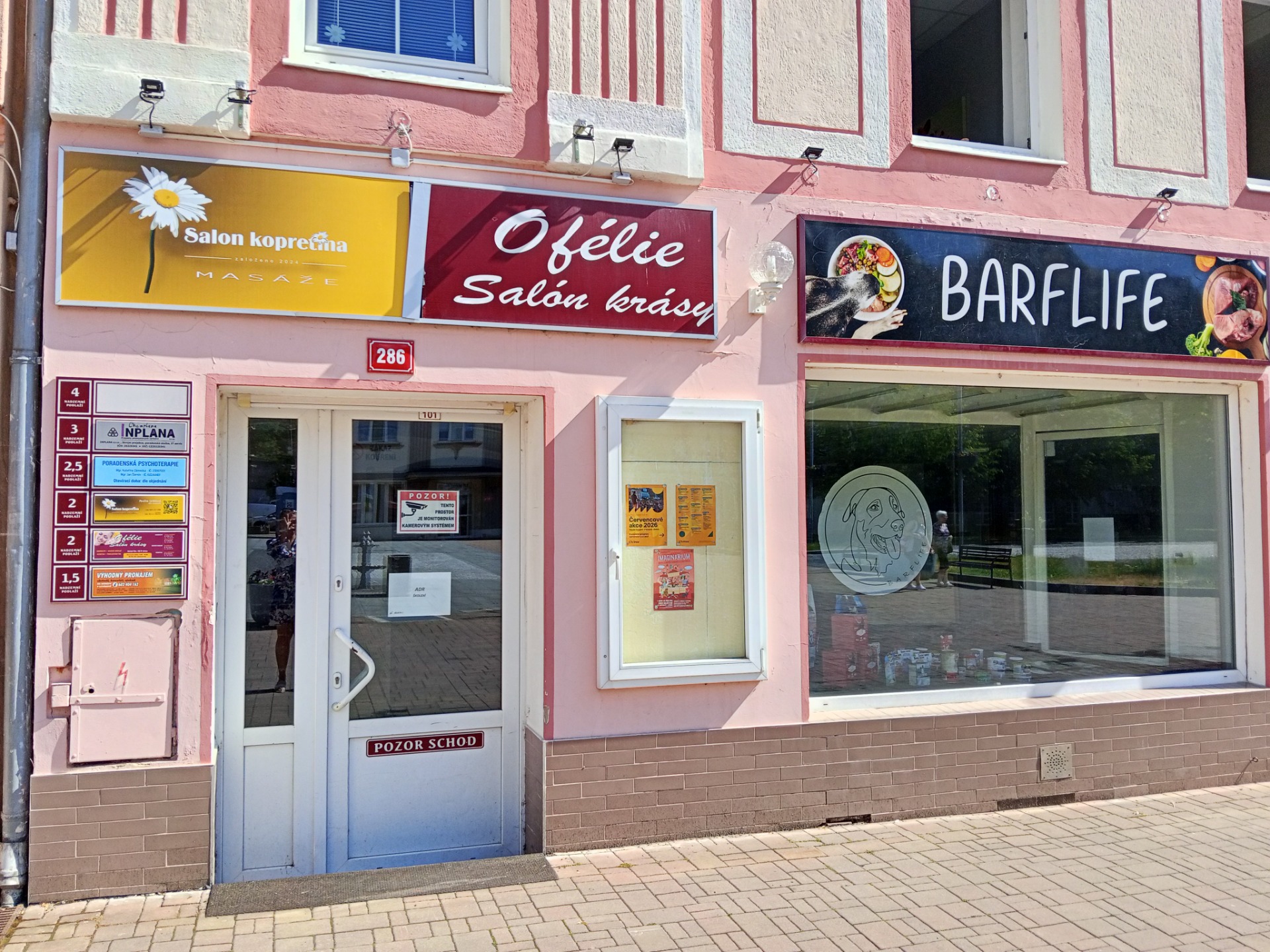 Vchod do budovy s reklamními tabulemi salonu, nápisem Ófélie, BARFLIFE a prosklenými dveřmi.